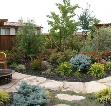 A serene landscape design customized by a landscape company in Vacaville, CA by Turfworks Inc, featuring a stone pathway, plants, and a fire pit area.
