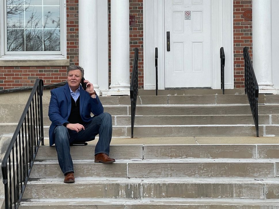 A man is sitting on the steps of a building talking on a cell phone.
