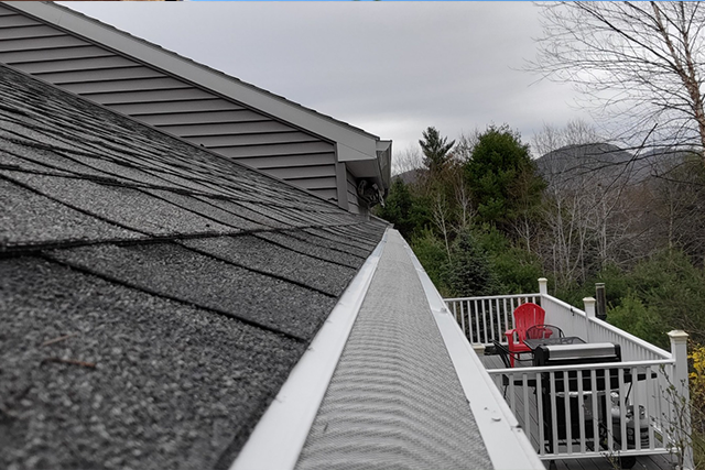 Gray roof with white gutters and a deck in the background, overcast day.