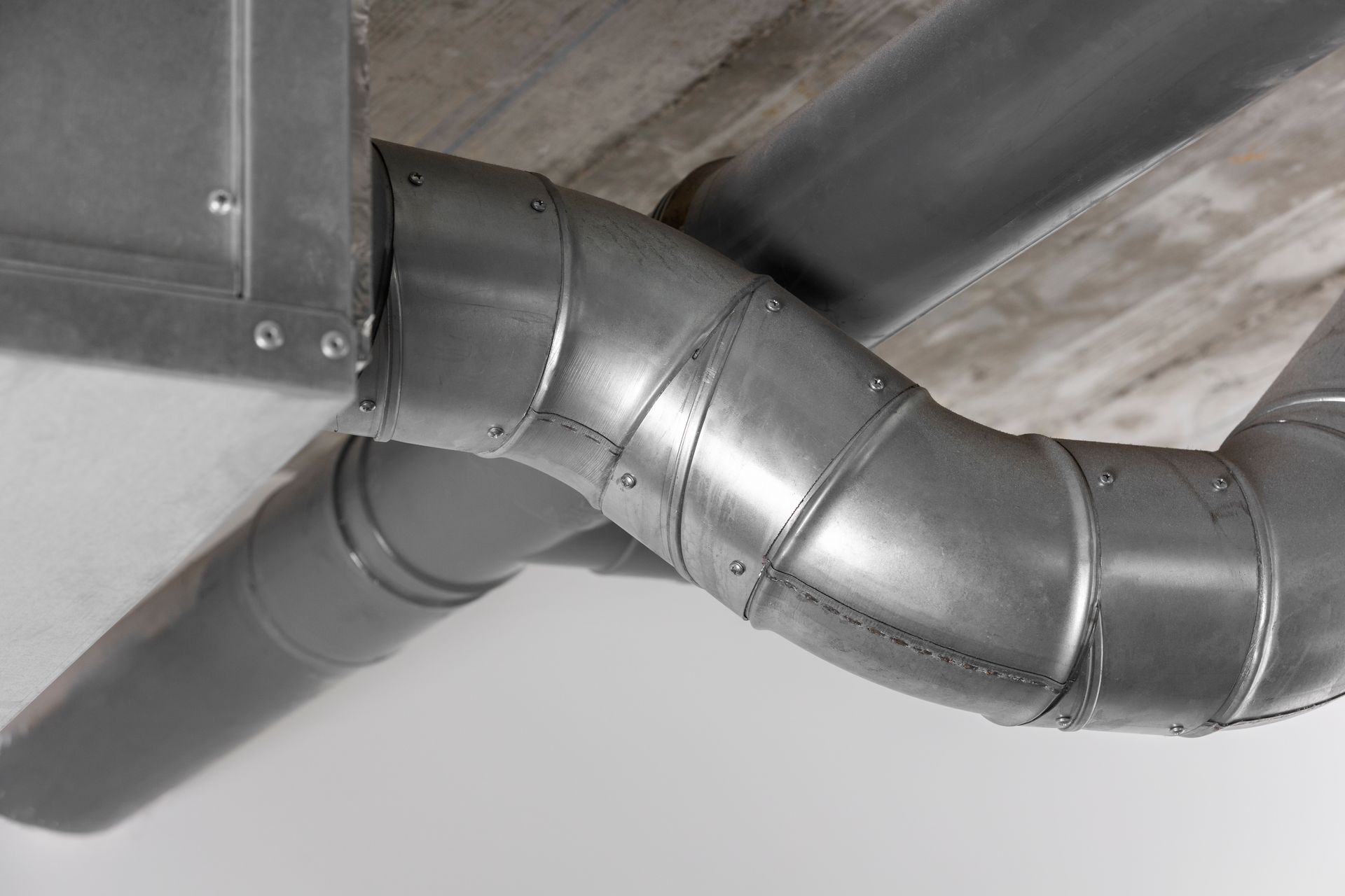 Metal ductwork angled across a white ceiling, with rivets visible.