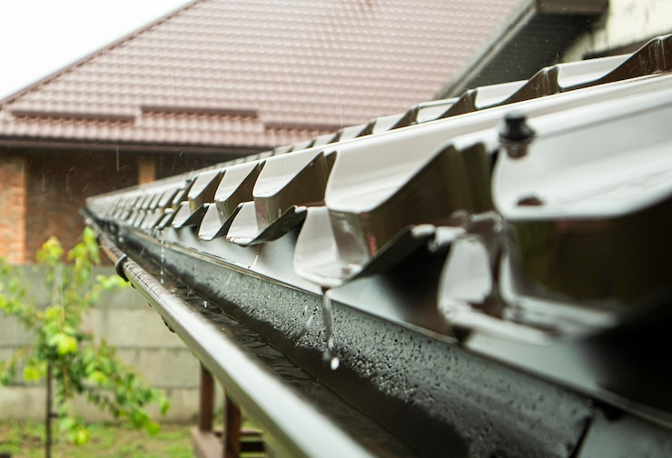 Brown rain gutter on a house roof during a rainy day.