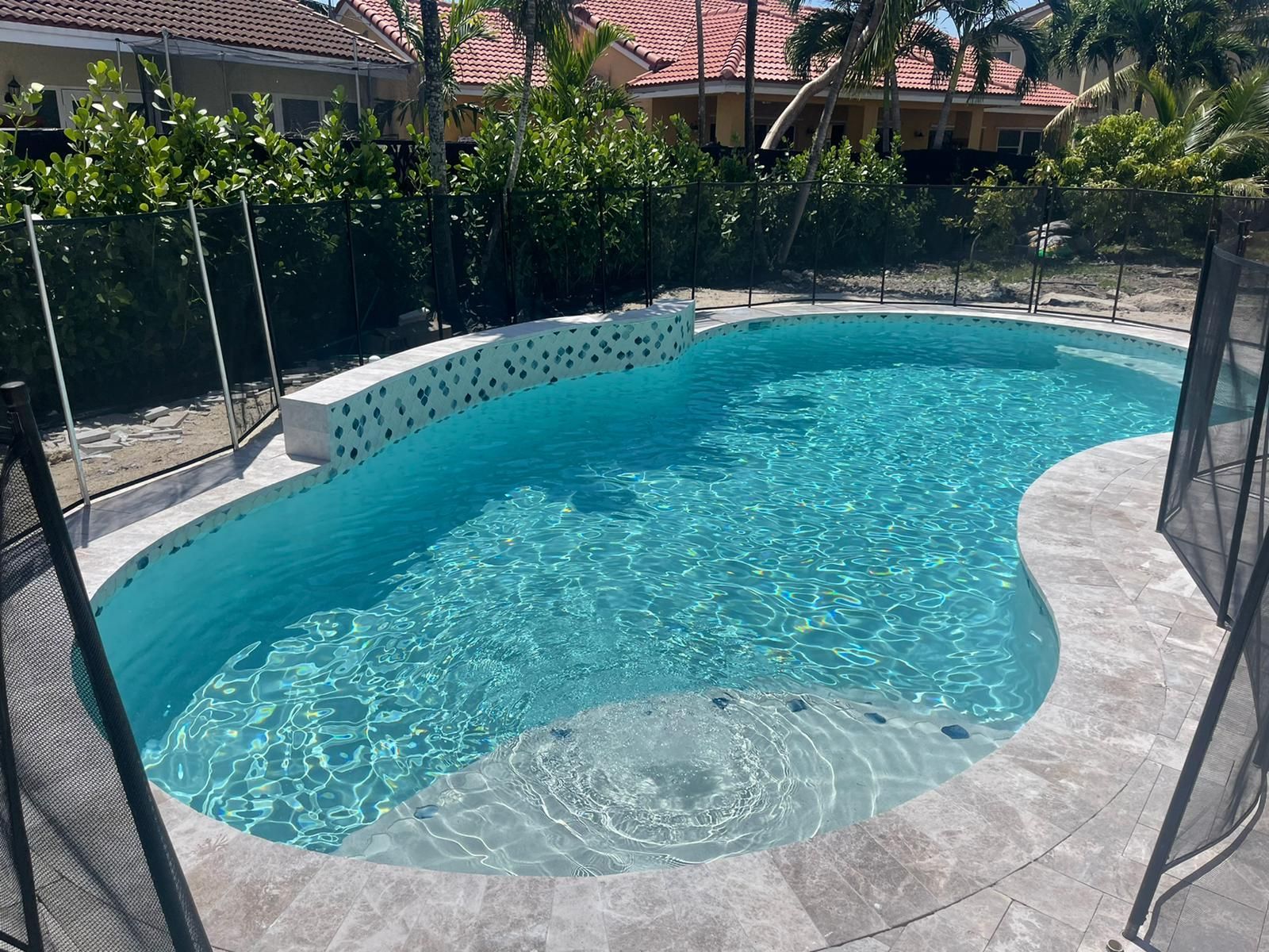 A large swimming pool is surrounded by a fence and a house.