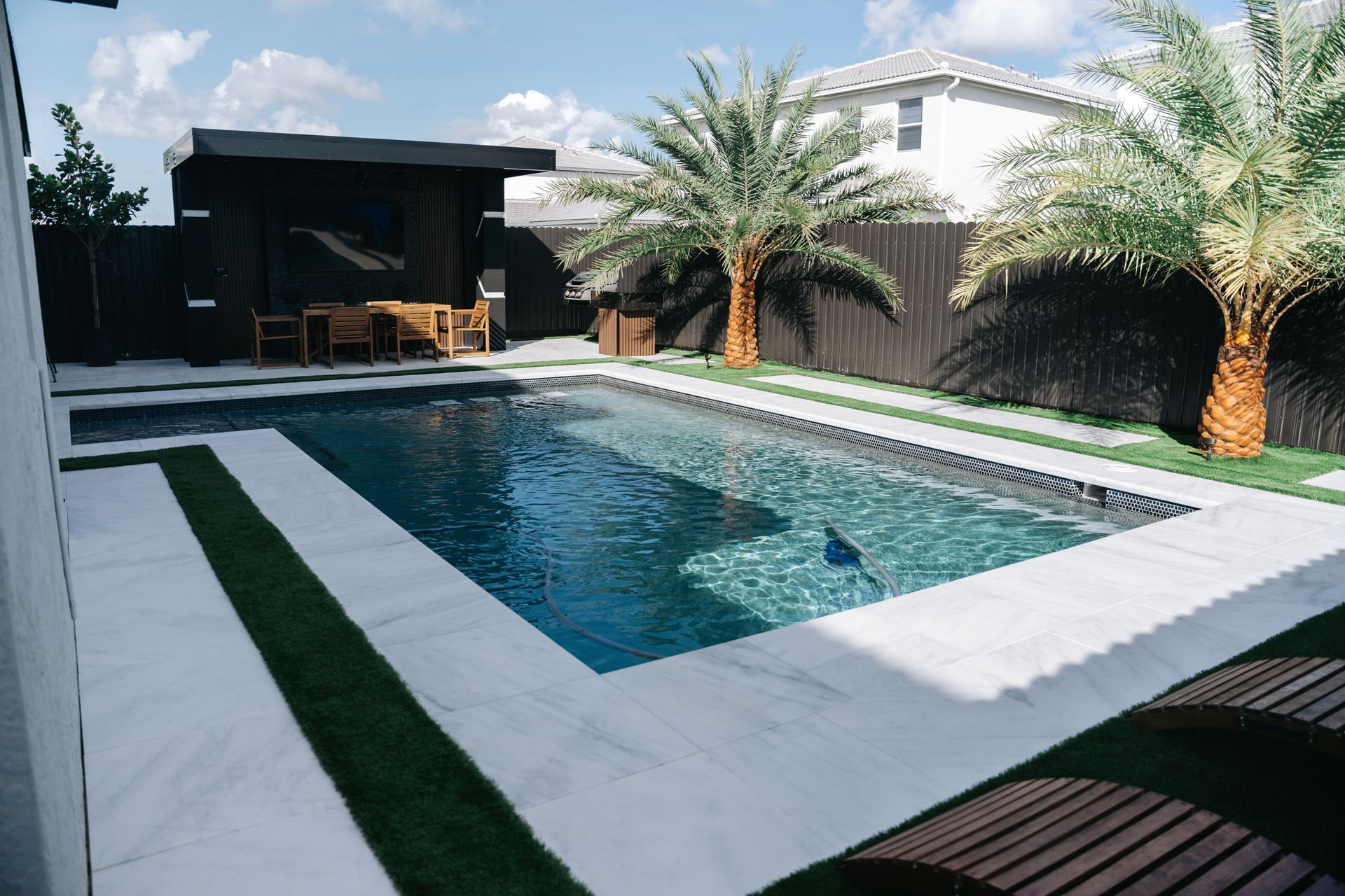 A large swimming pool in the backyard of a house surrounded by palm trees.