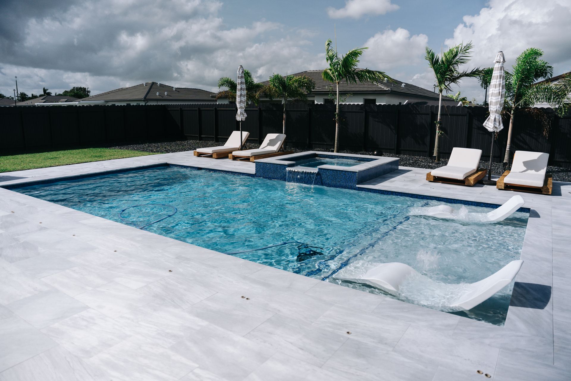 A large swimming pool with chairs and umbrellas in a backyard.