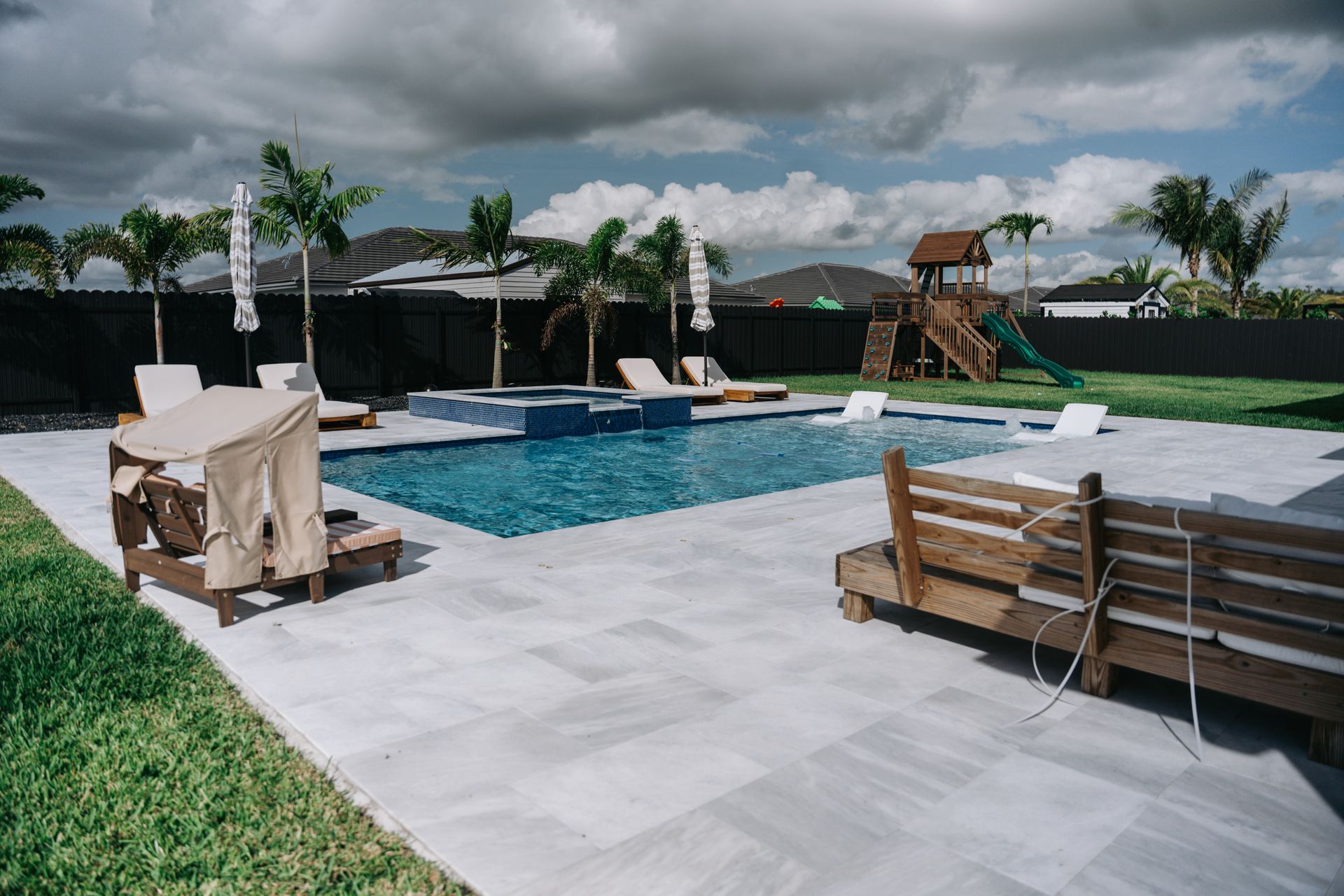 There is a large swimming pool in the backyard with a playground in the background.