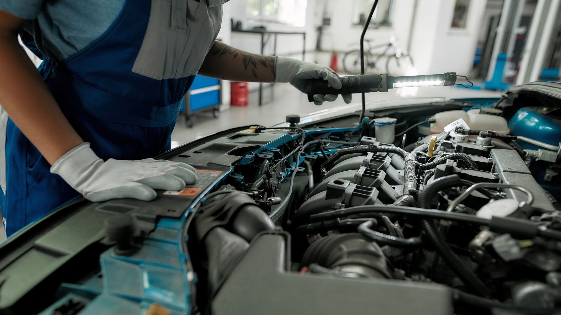 Close-up of a car’s engines and motor as a car mechanic checks it with a light, the car’s hood up.