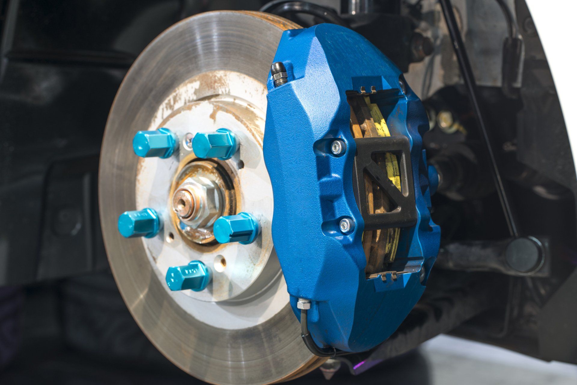Blue brake caliper on a car's rotor with blue lug nuts.