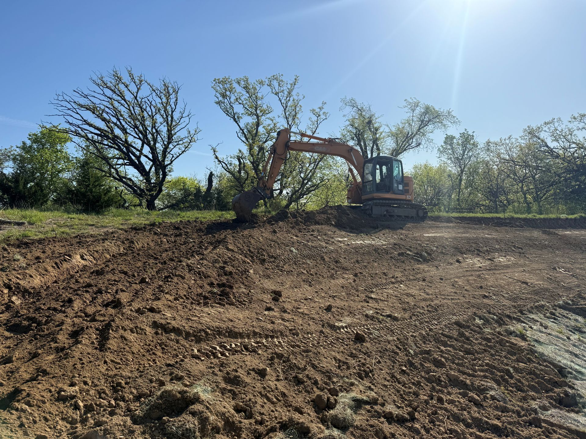 A white Bobcat excavator digs a trench in a dirt area, with a truck trailer visible in the background.