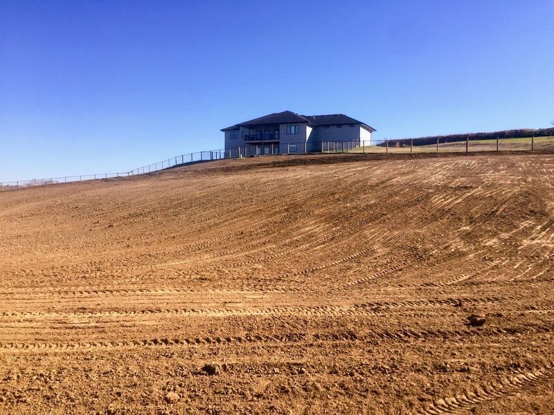 House on a bare, brown hill under a clear blue sky. A fence runs along the top.