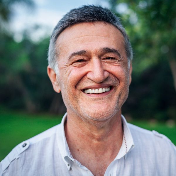 Smiling man in a white shirt outdoors with a blurred green background