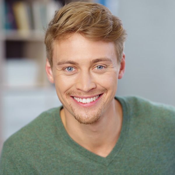 Smiling person in a green sweater against a blurred indoor background