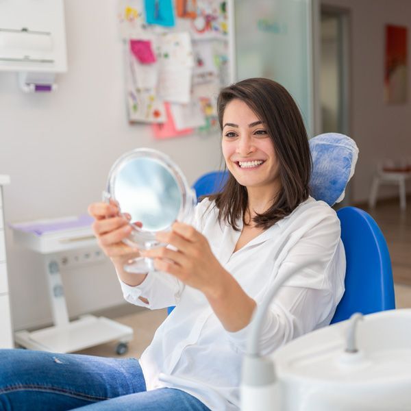Smiling patient holding a mirror while reclining in a dental chair during a dental exam