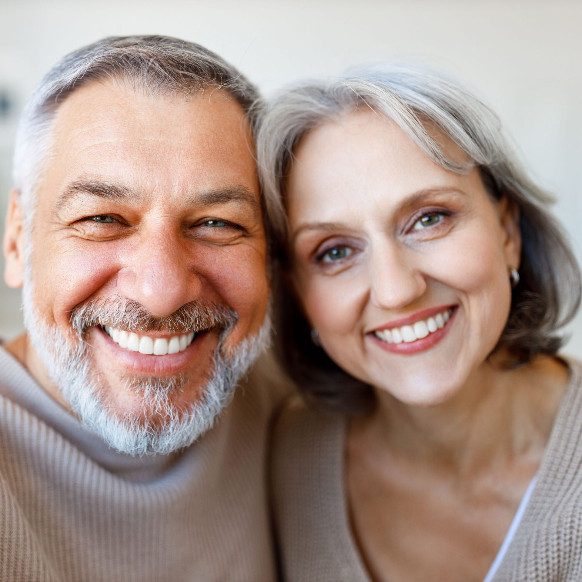 Two smiling people in sweaters, posing closely together against a light background