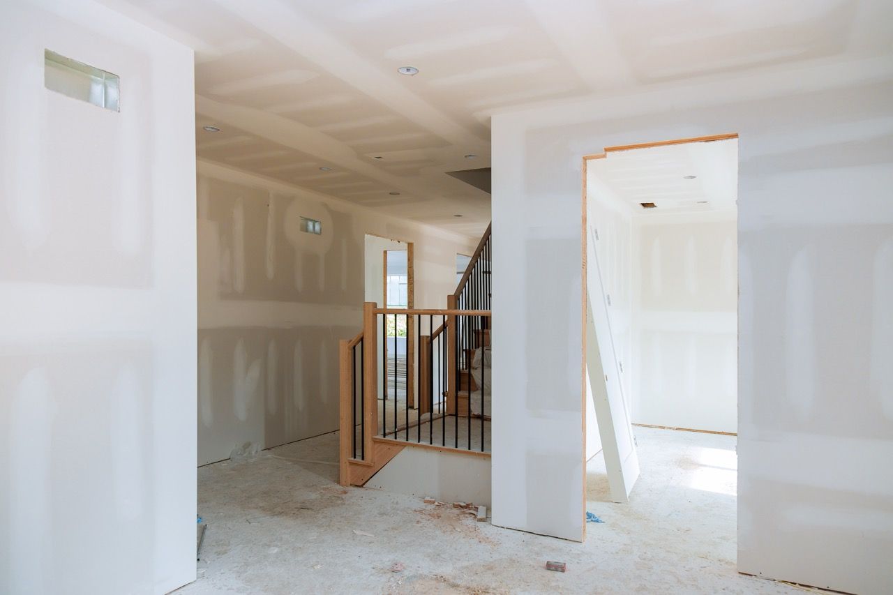 Unfinished hallway with drywall, exposed stair railing, and a bright open doorway.