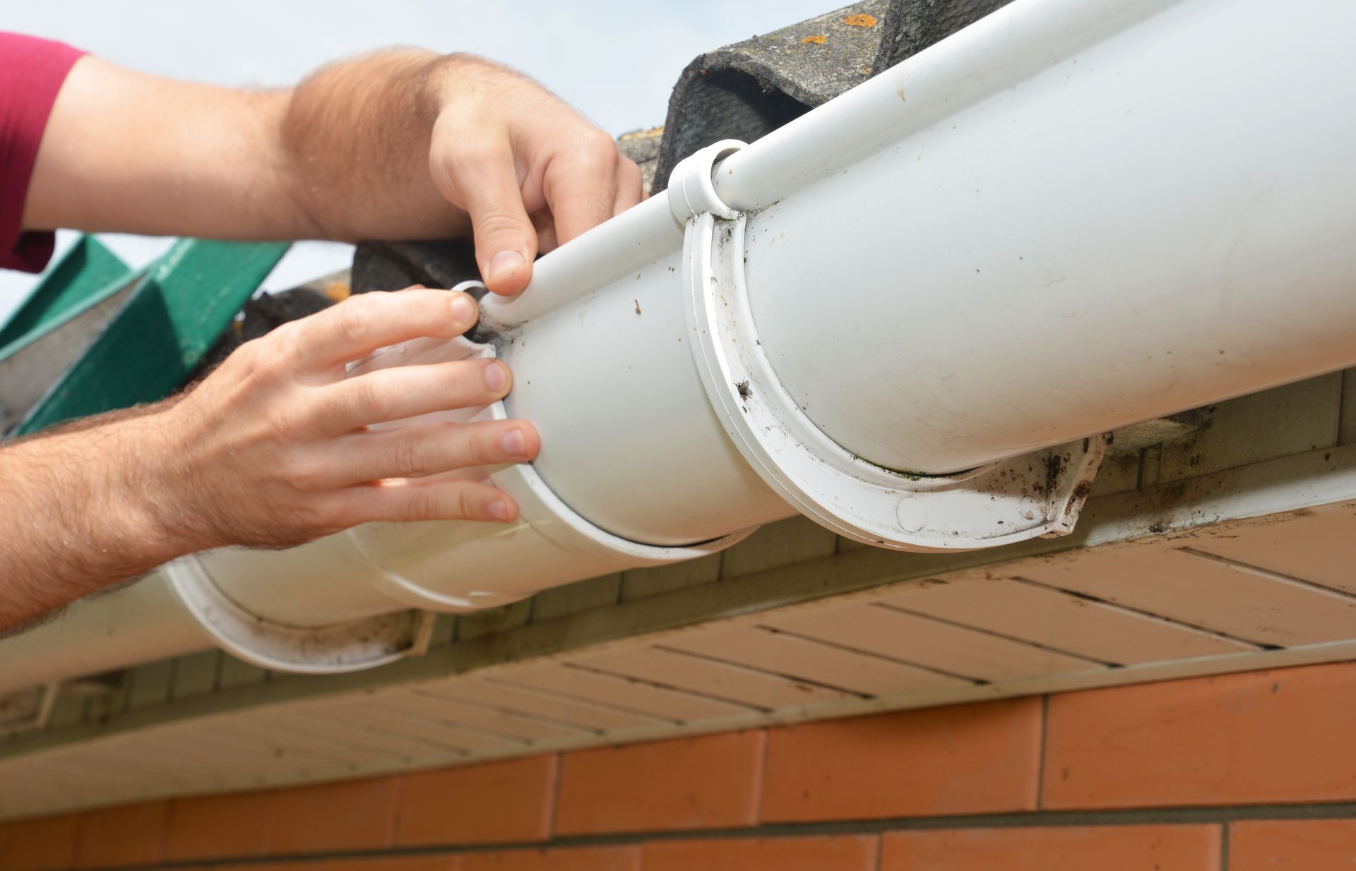 A man is fixing a gutter on the roof of a house.
