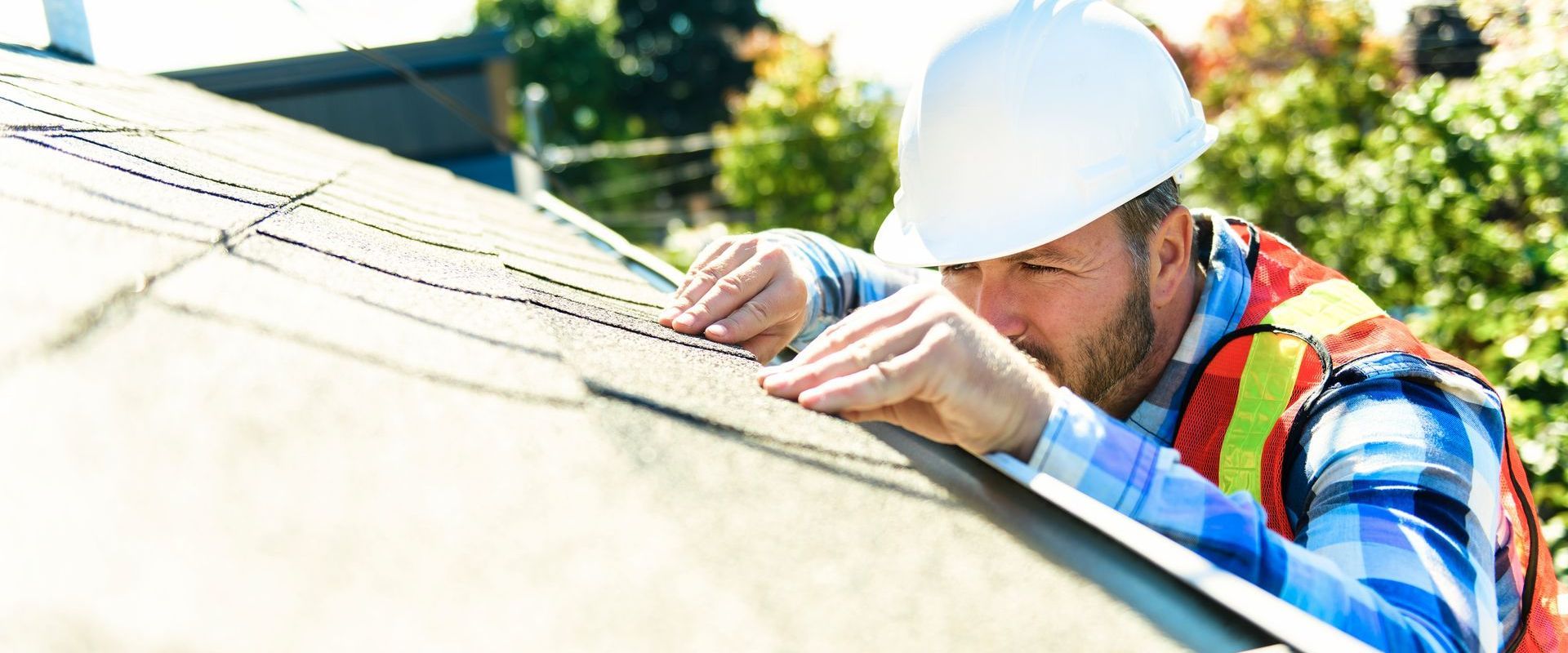 A man wearing a hard hat and safety vest is working on a roof.