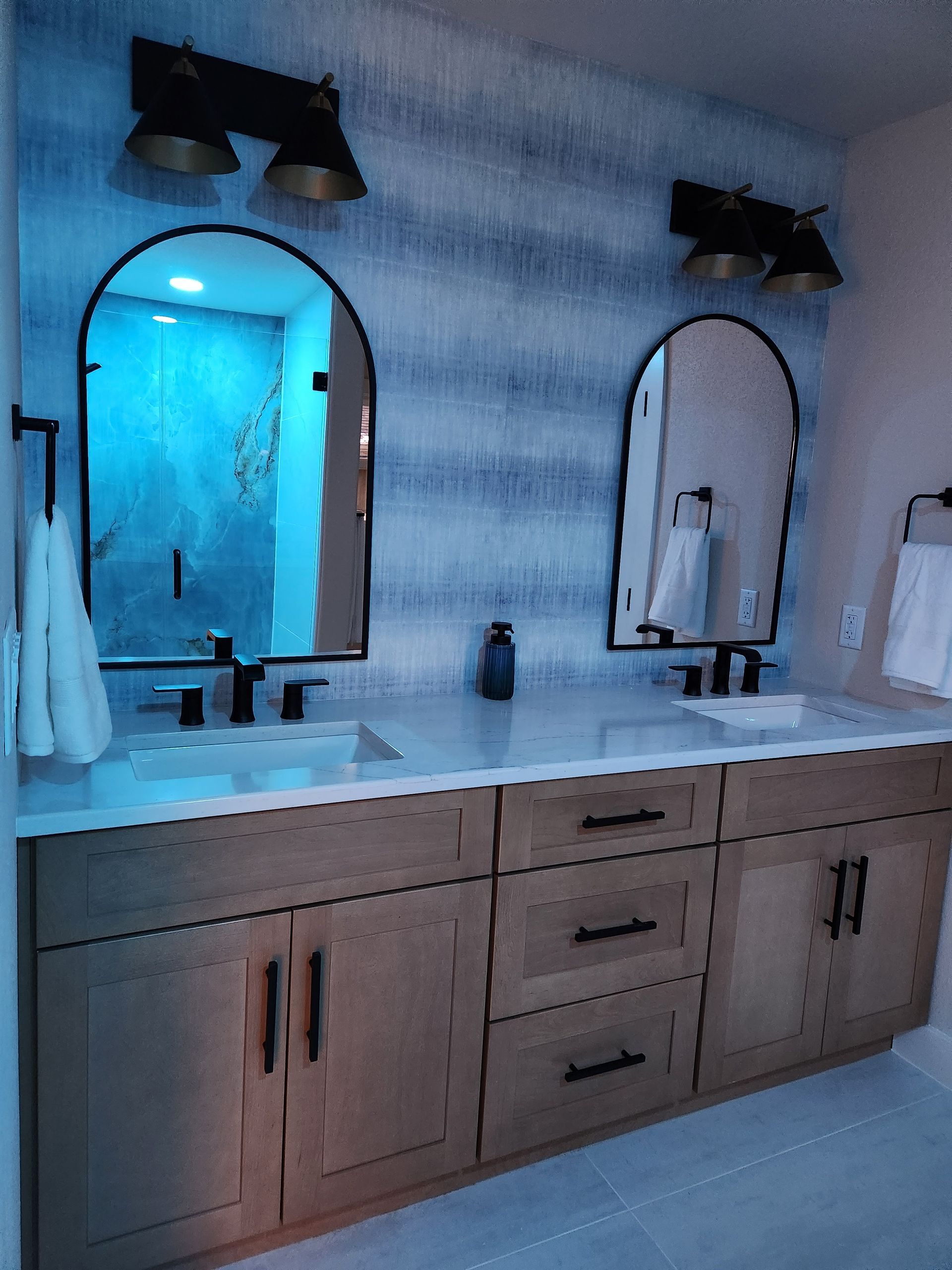 Bathroom with light wood vanity, arch mirrors, blue accent wall, and black fixtures.