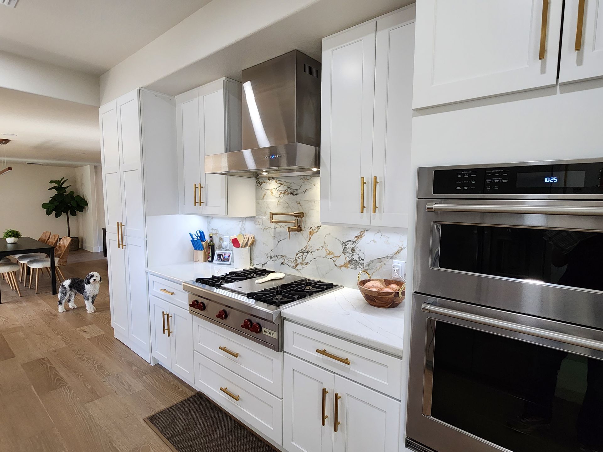 Modern white kitchen with stainless steel appliances, marble backsplash, and hardwood floors.
