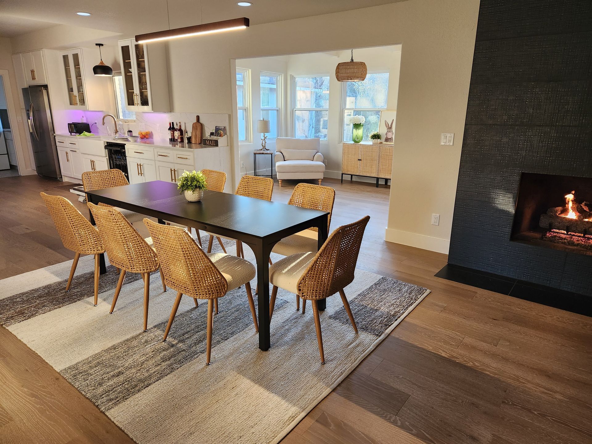 Dining room with table, woven chairs, rug, fireplace, and a view to a living area.