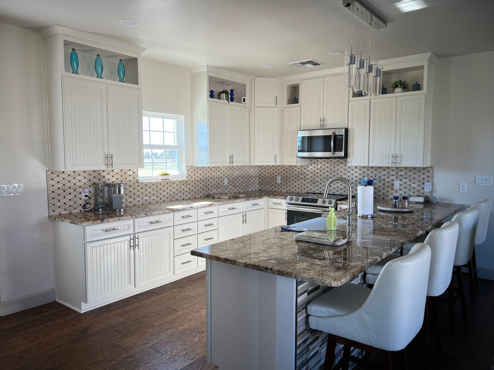 Bright white kitchen with granite countertops, white cabinets, and bar seating.