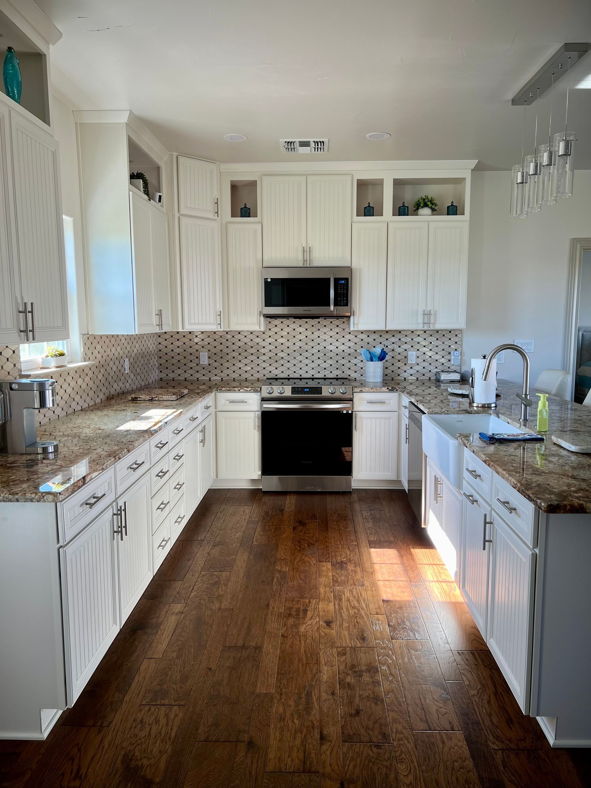 White kitchen with dark wood floor, granite countertops, and stainless steel appliances.