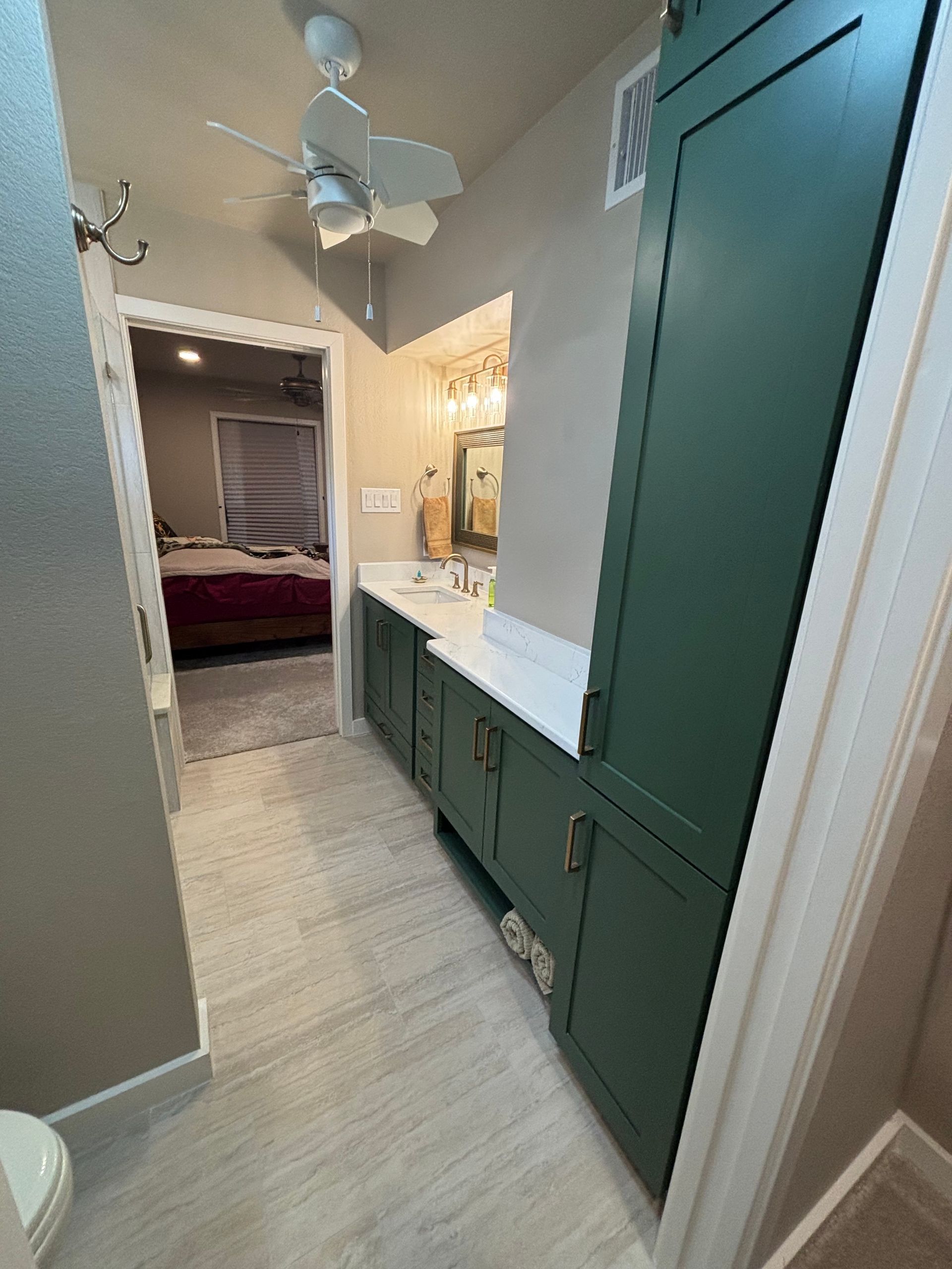Bathroom with green cabinets, white countertop, and doorway to bedroom.