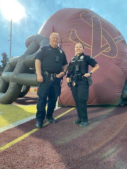 Two police officers standing on a track, a large football helmet in the background.
