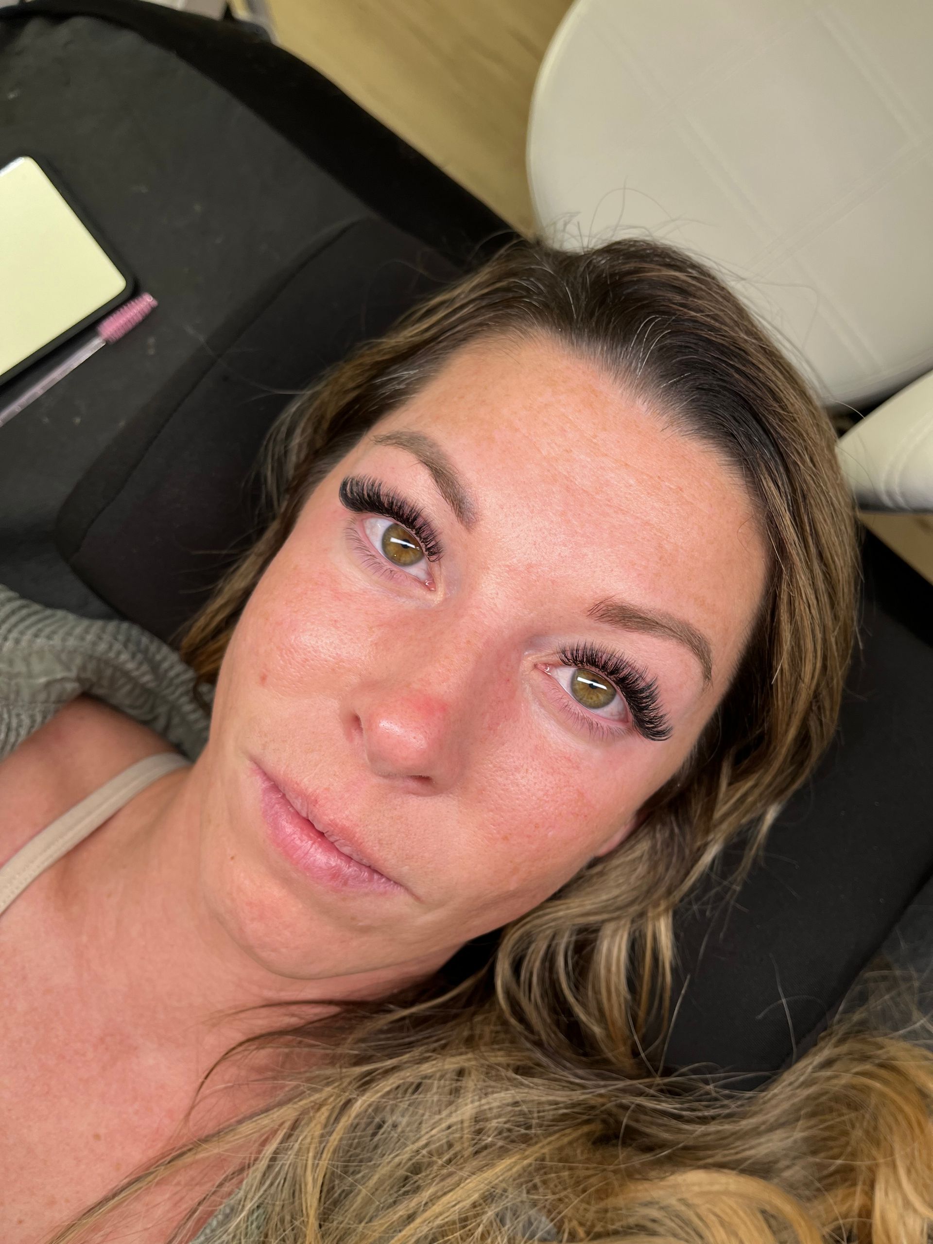 Close-up of a woman lying on a dark cushion, wearing a beige top and looking at the camera.