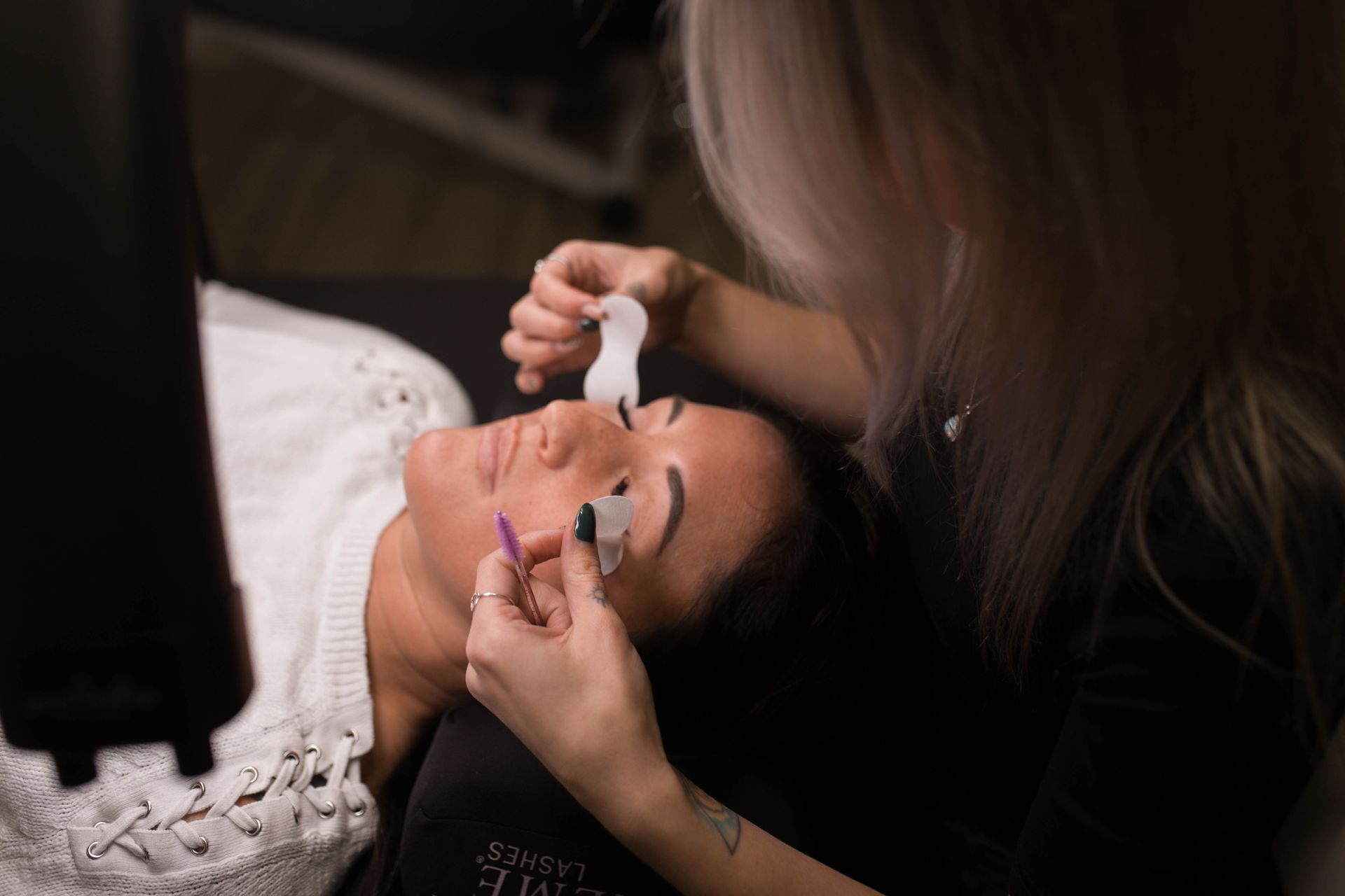 Person lying down while another applies eye drops in a dimly lit setting