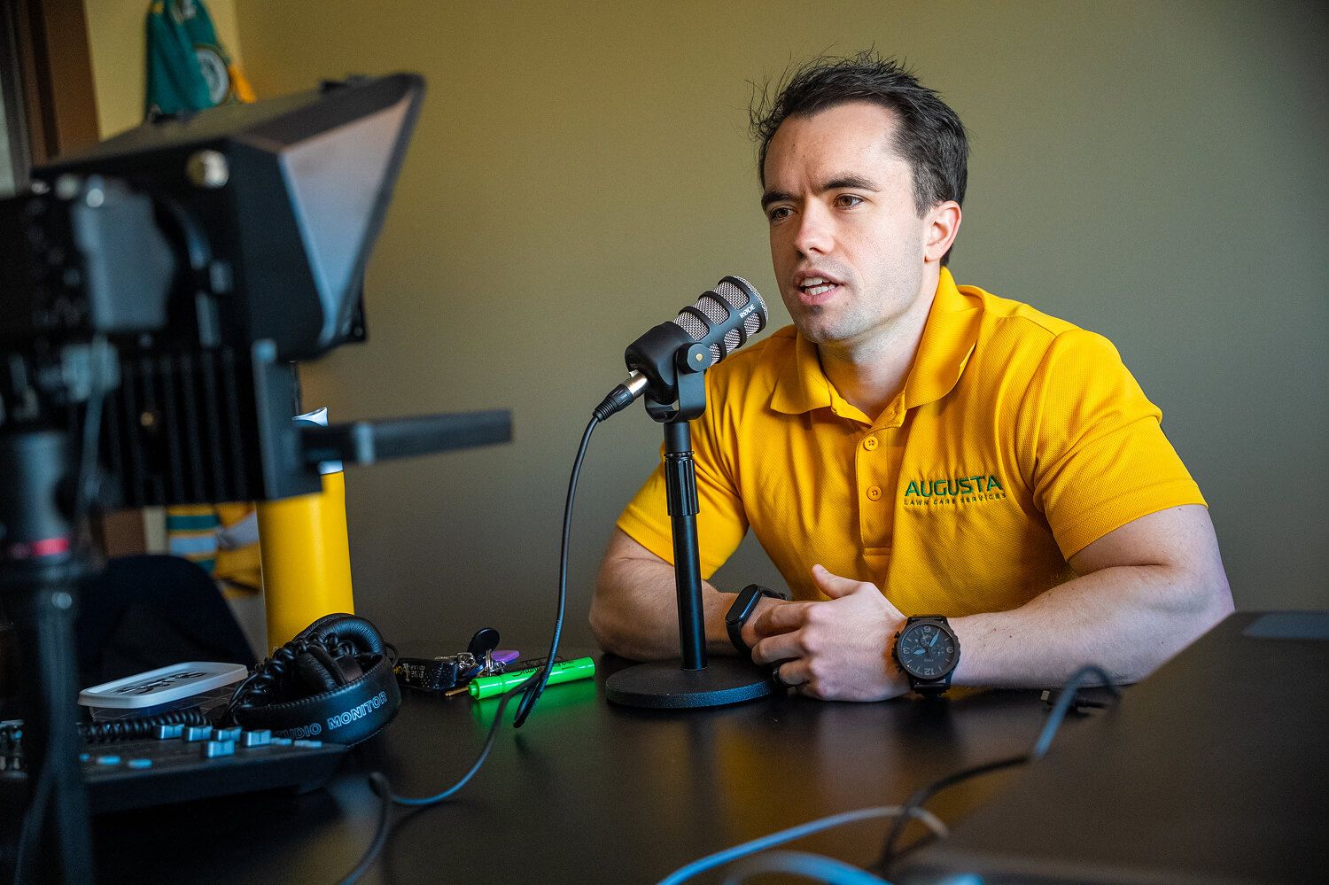 Man speaking into a microphone at a desk with recording equipment in a studio setting