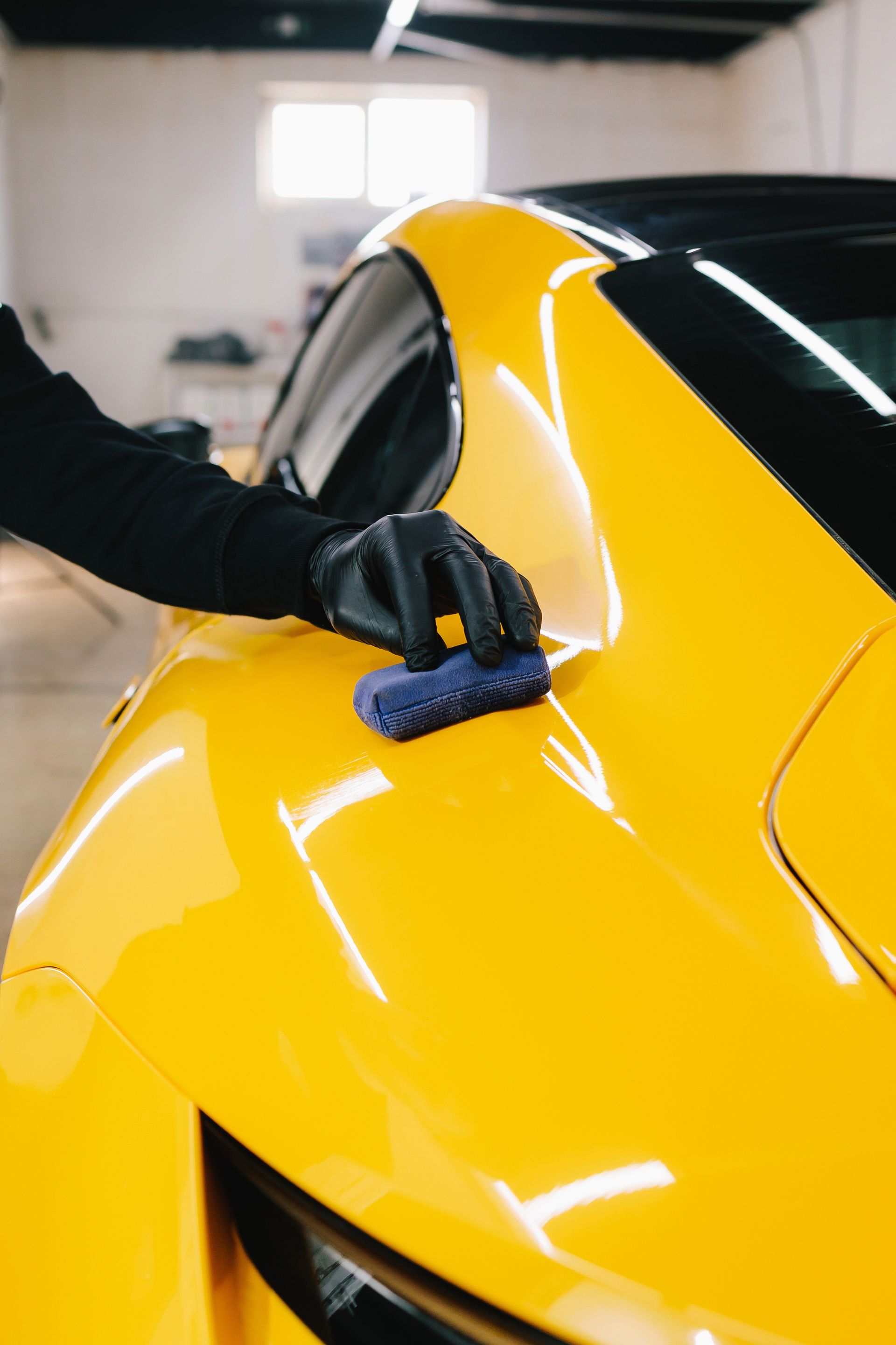 Gloved hand polishing a bright yellow car in a garage