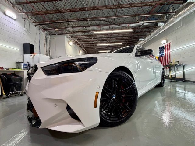 White sports car in a garage, shown from the front-left with black rims and a low stance.