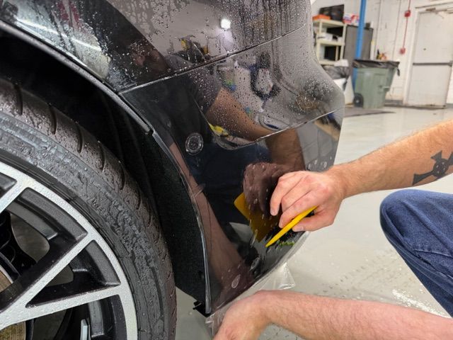 Technician using a yellow tool to repair a black car’s rear body panel in a garage