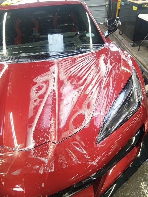 Red car hood covered in a clear protective film inside an auto shop