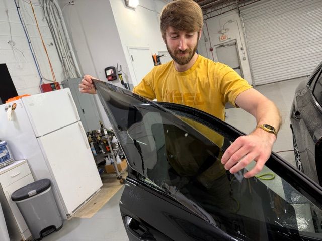 Person in a yellow shirt adjusting a car window tint in an auto shop