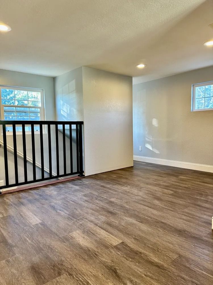 Interior view of a room with wood-look flooring, light gray walls, and a black railing.