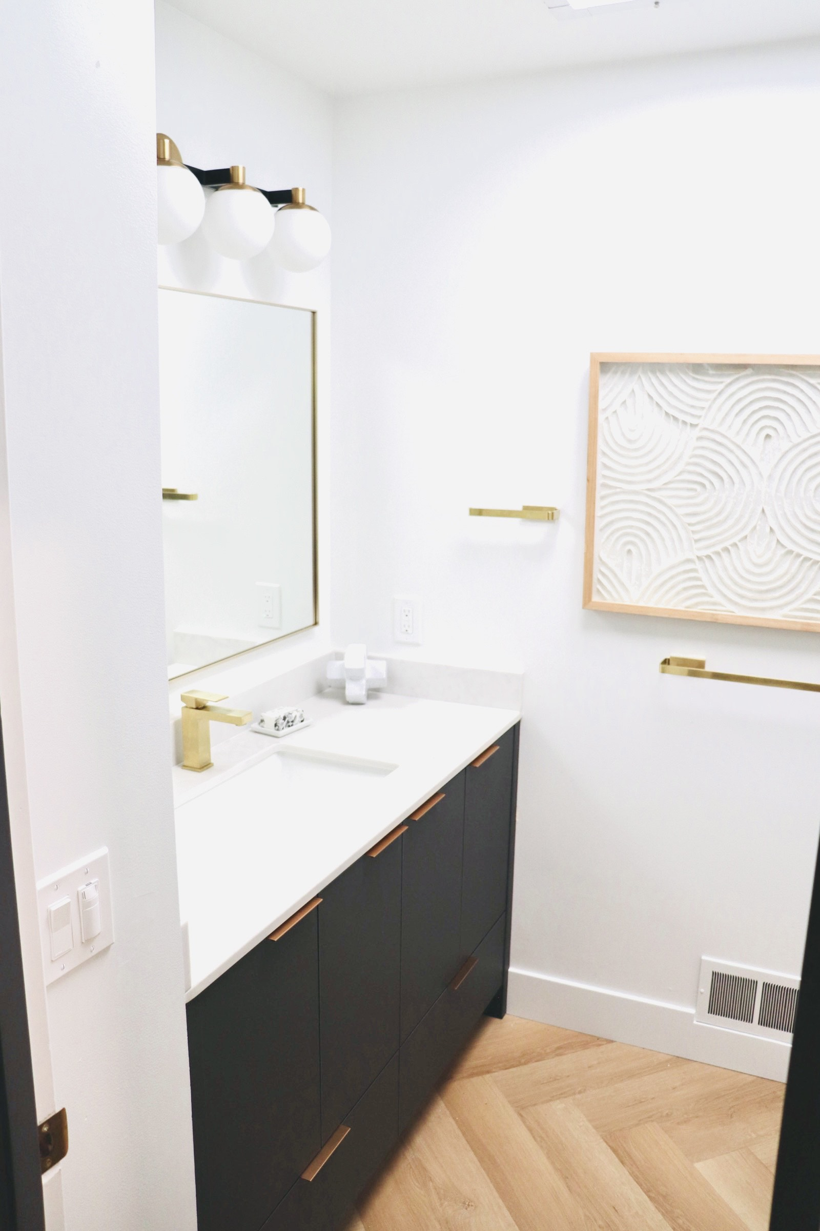 Small bathroom with black vanity, gold fixtures, white countertop, and decorative art.