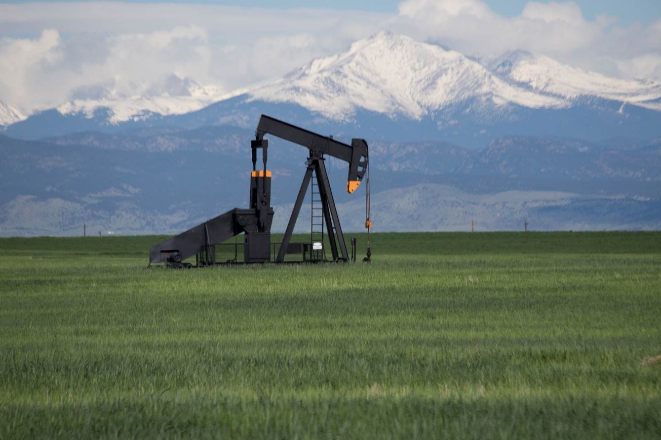 Oil pumpjack in a green field with snow-covered mountains in the background.