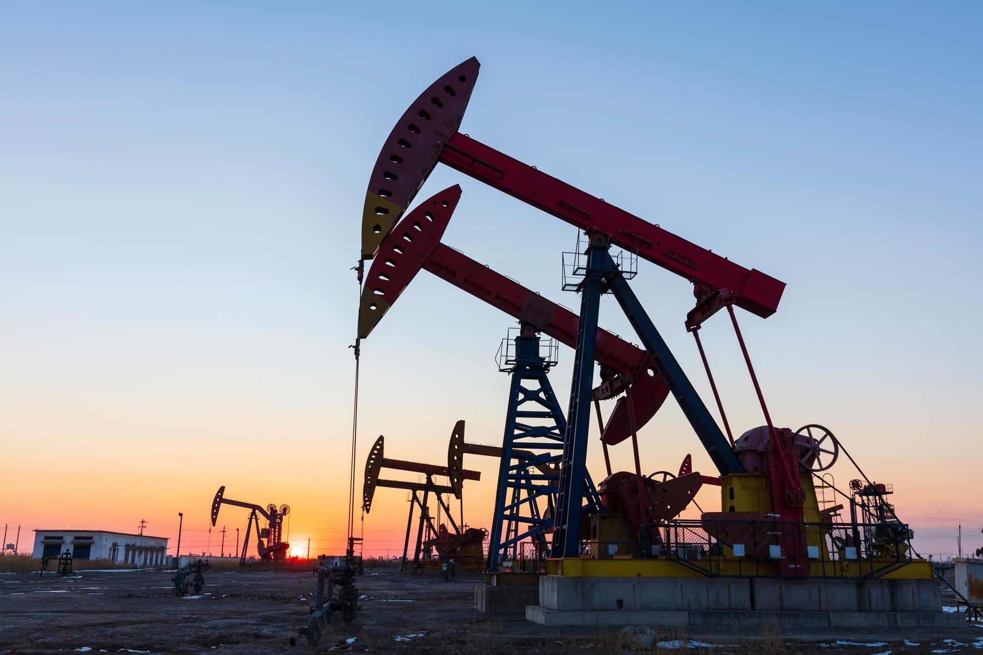 Oil pump jacks silhouetted at sunset in an industrial field