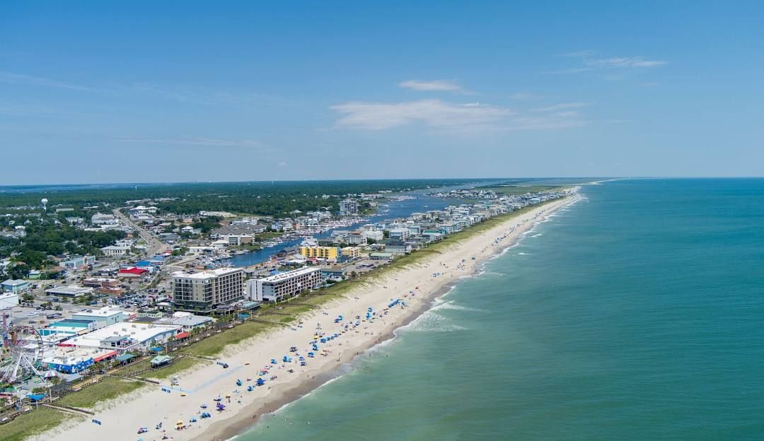Aerial view of a sandy beach with ocean on the right and buildings lining the coast on the left.