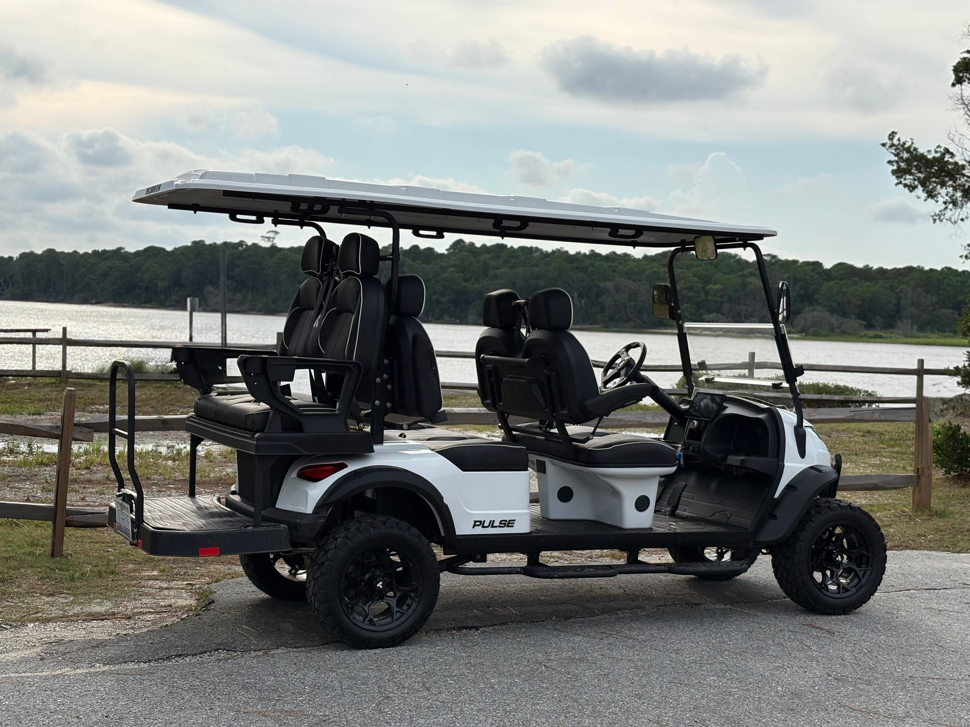 Golf cart parked by a lakeside with fishing gear and seating under a canopy.