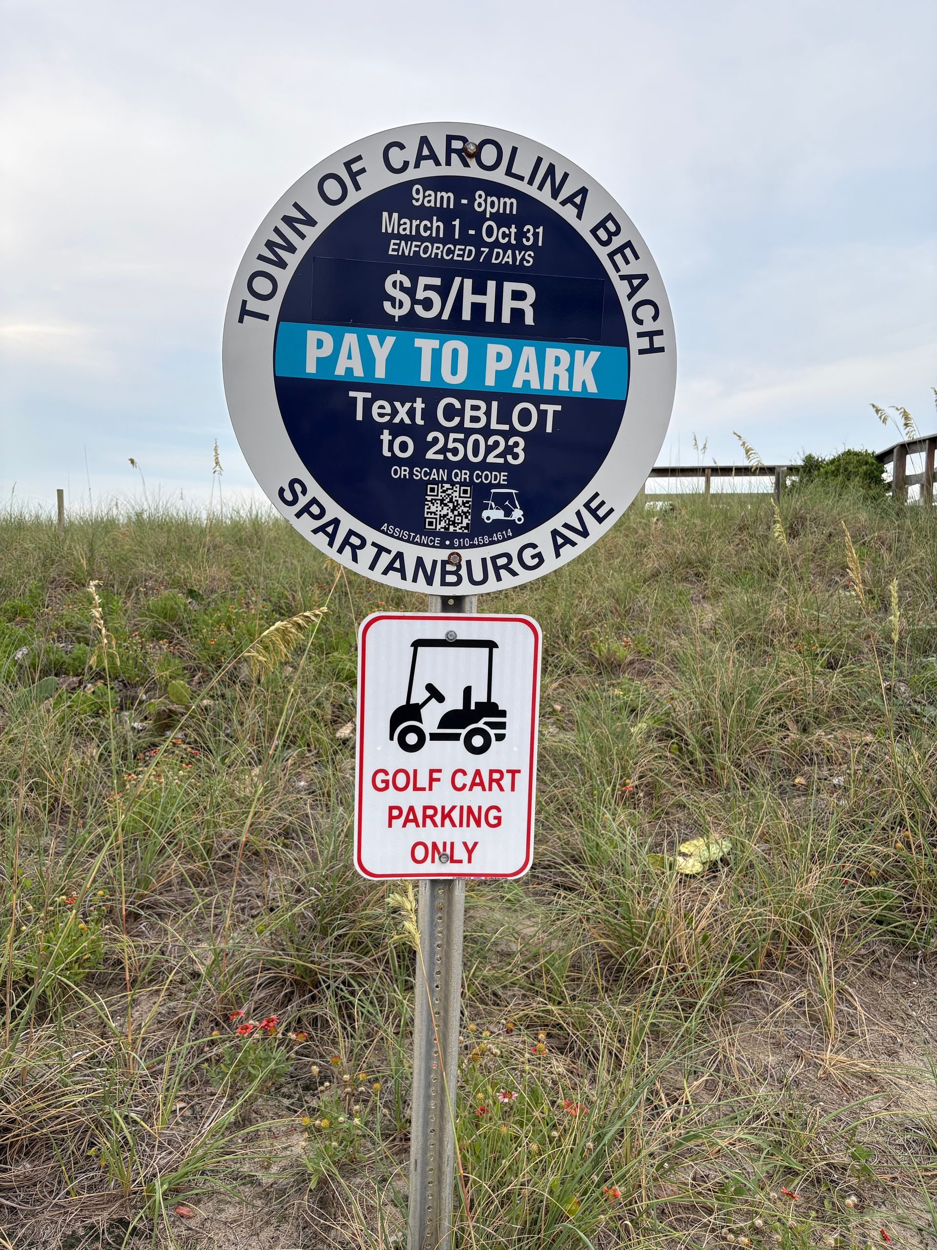 Carolina Beach pay-to-park sign with a golf cart parking only sign below, in a grassy roadside area