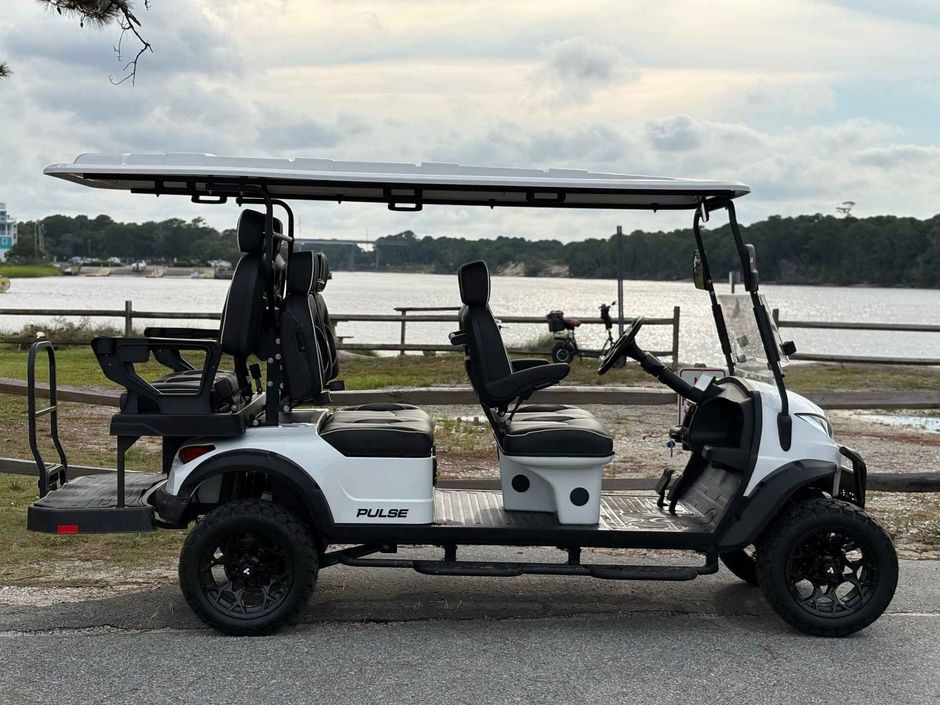 White golf cart with roof parked beside a waterfront road under cloudy sky