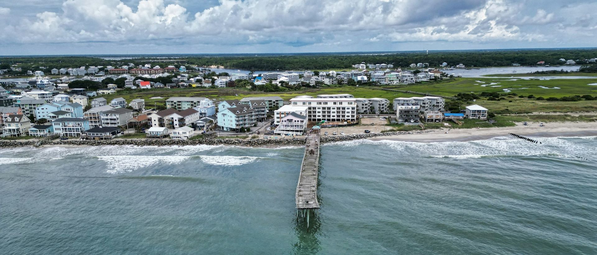 Aerial view of a coastal town with a pier extending into the ocean under cloudy skies