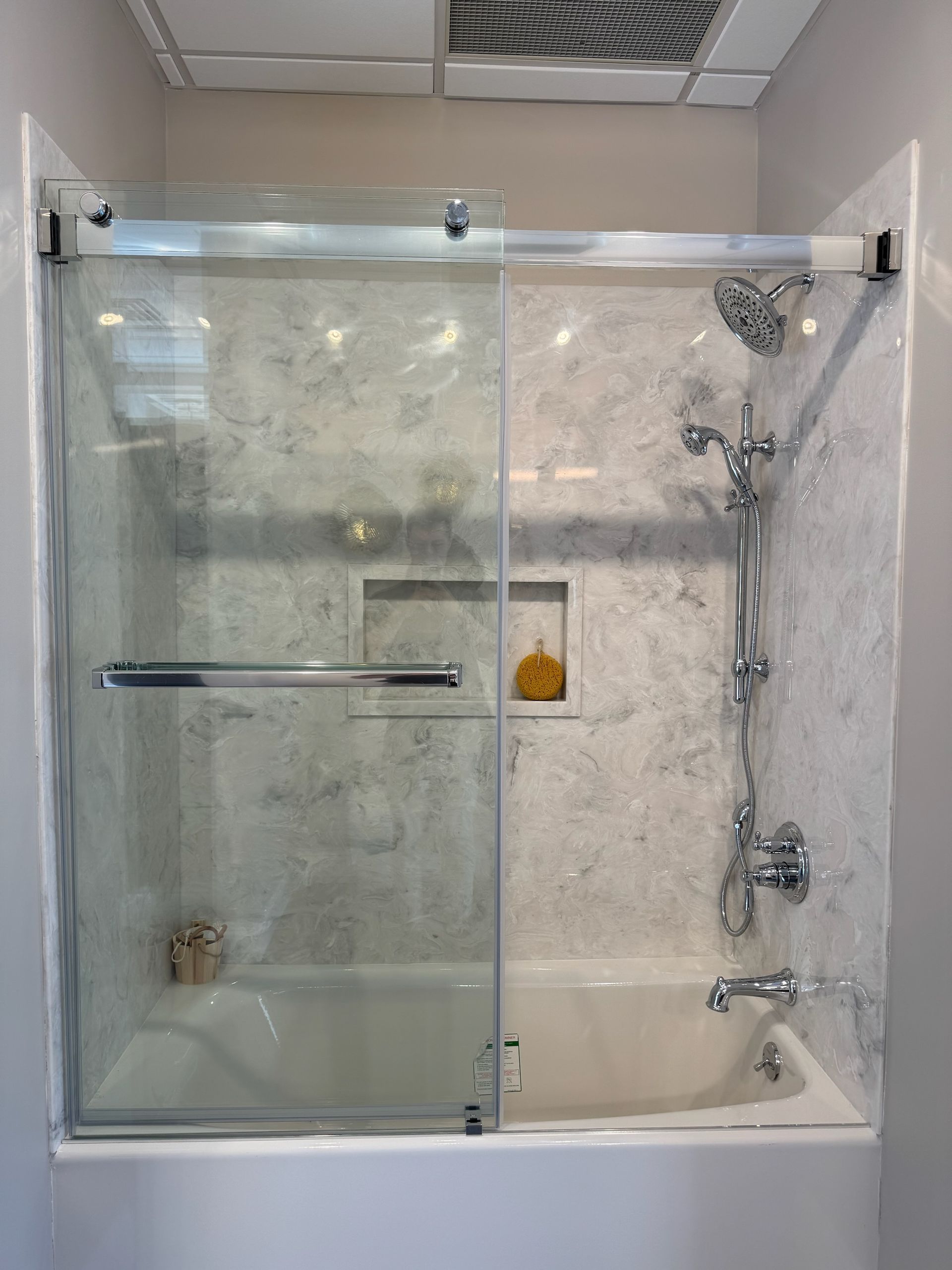 Accessible shower with grab bars, handheld showerhead, bench, and recessed niche on light tile walls.