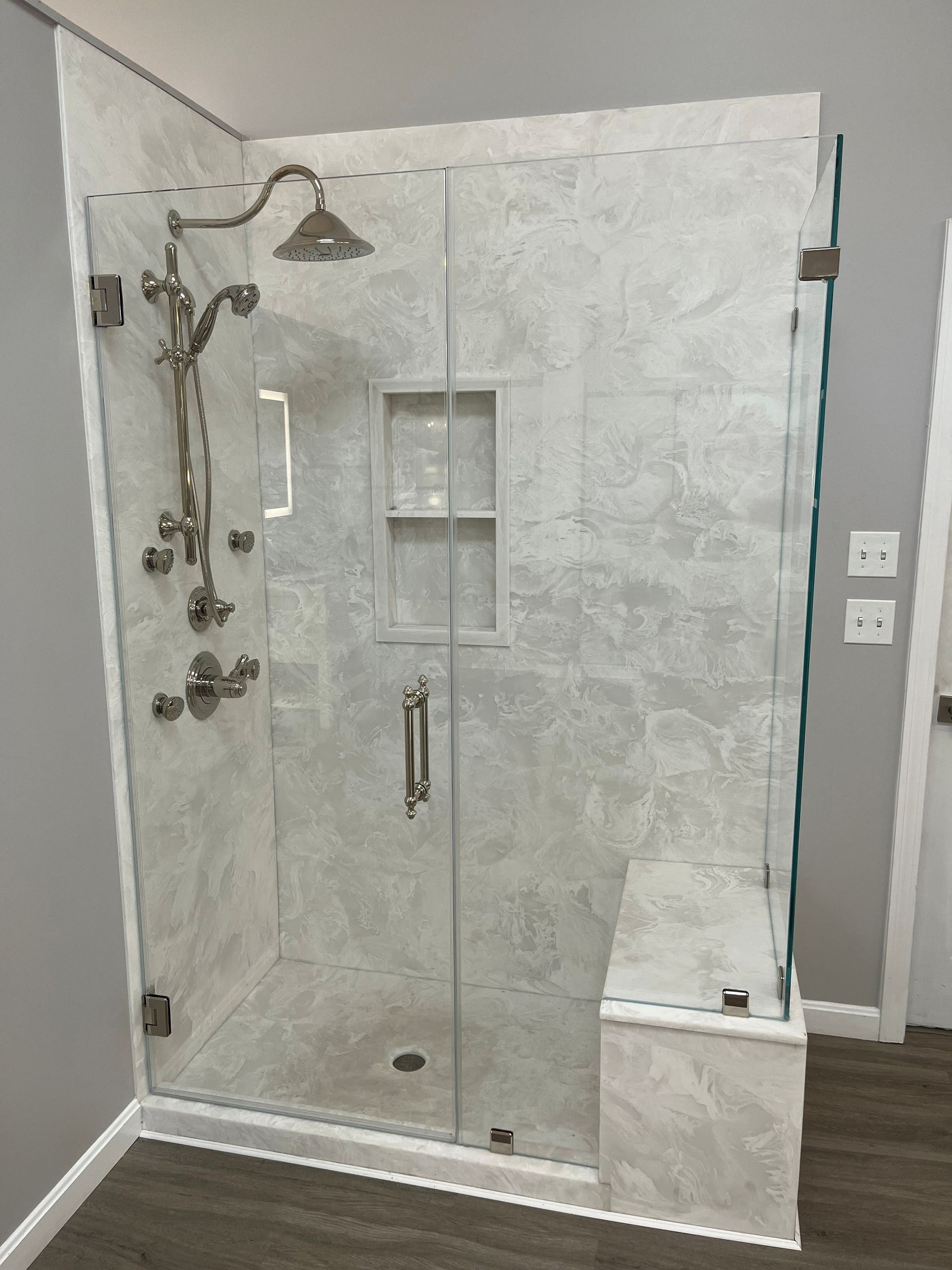 Glass walk-in shower with marble tile, built-in shelf, and chrome shower fixtures in a bathroom