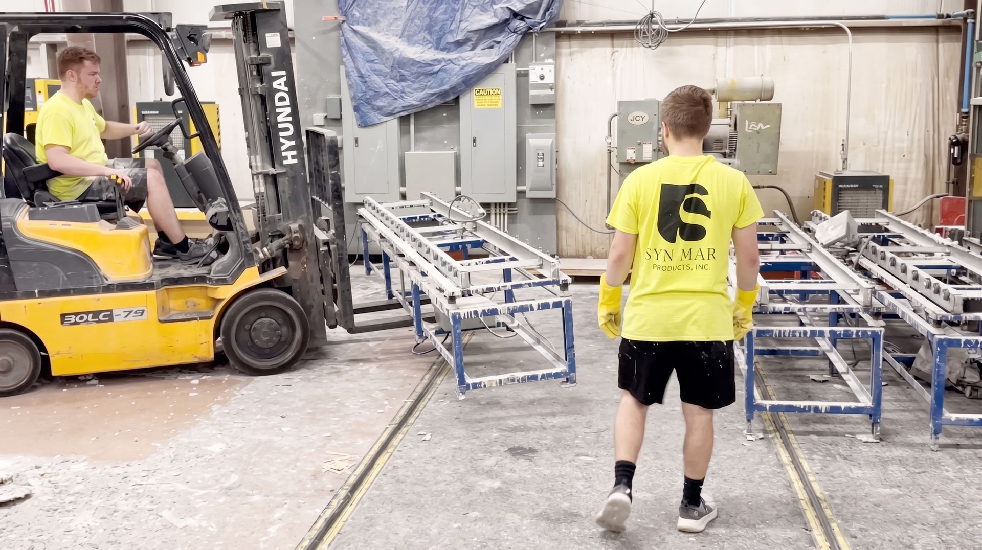 Forklift and worker in a warehouse beside rows of metal frames and equipment