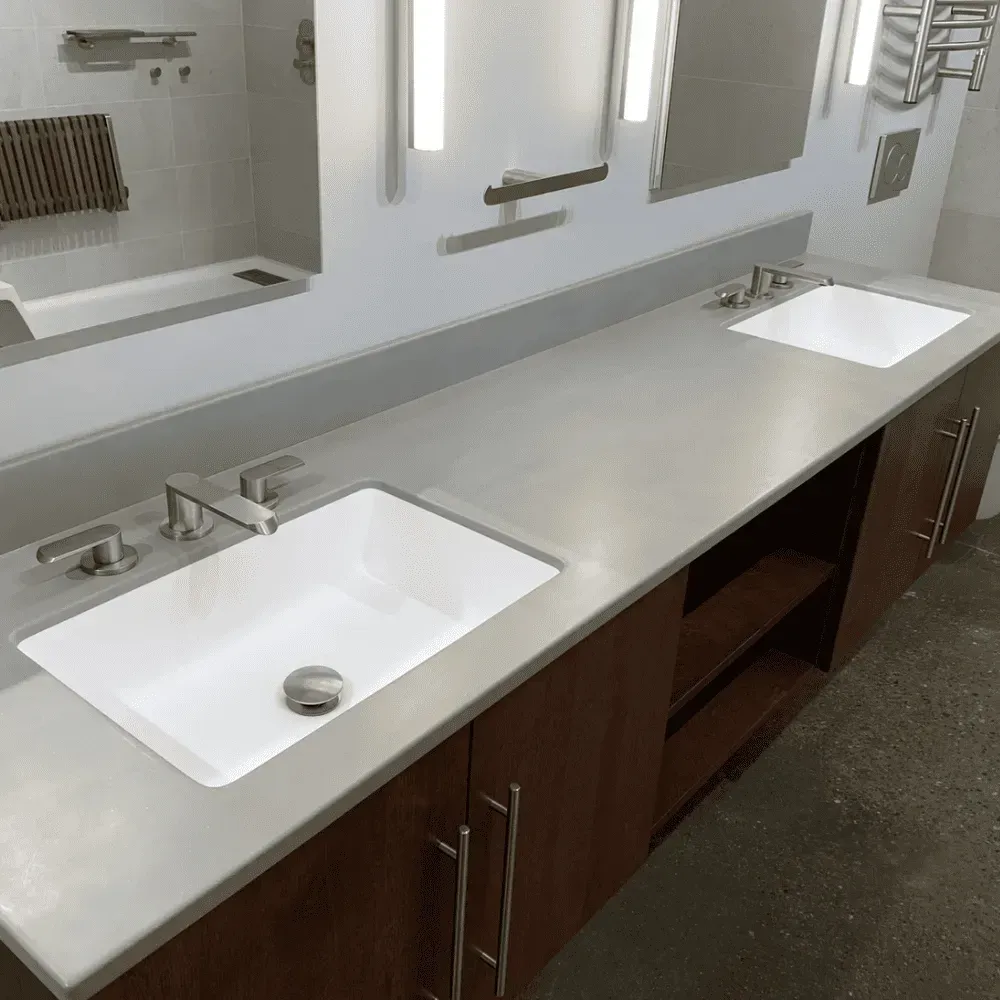 Accessible bathroom vanity with two white sinks, long gray countertop, and mirrors above a wood cabinet.