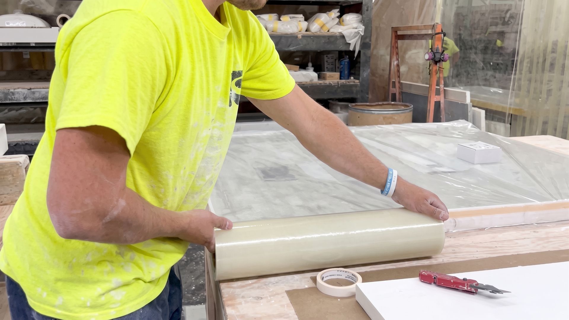 Worker in neon yellow shirt rolling material on a workbench in a workshop
