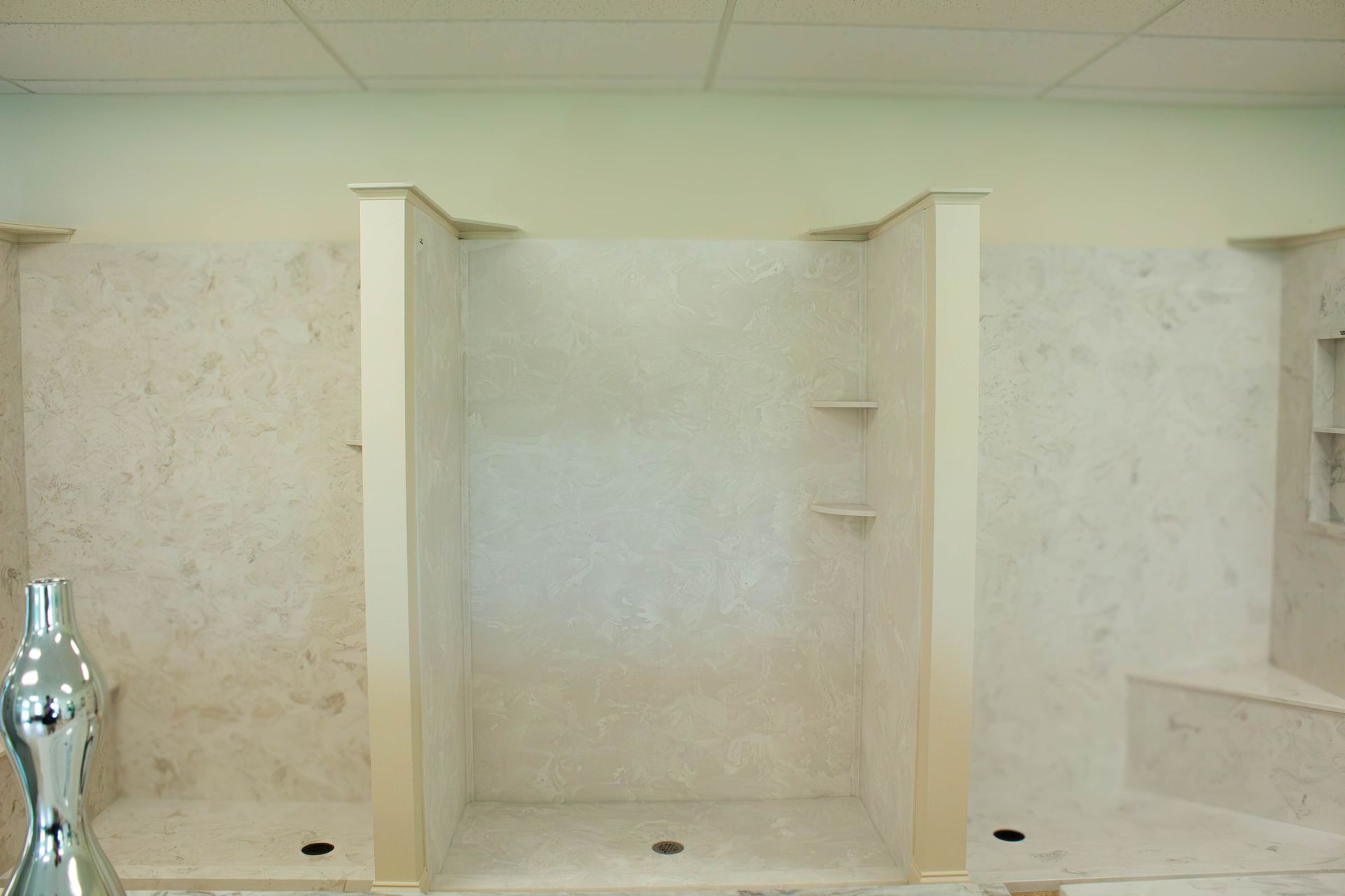 White tiled shower stall with built-in shelves, showerhead, grab bars, and a handheld sprayer.